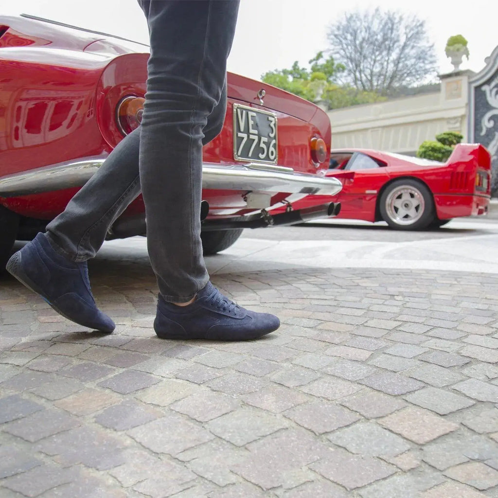 Paire de chaussures Sparco Imola en cuir suédé bleu, made in Italy, portée devant des voiture Italiennes