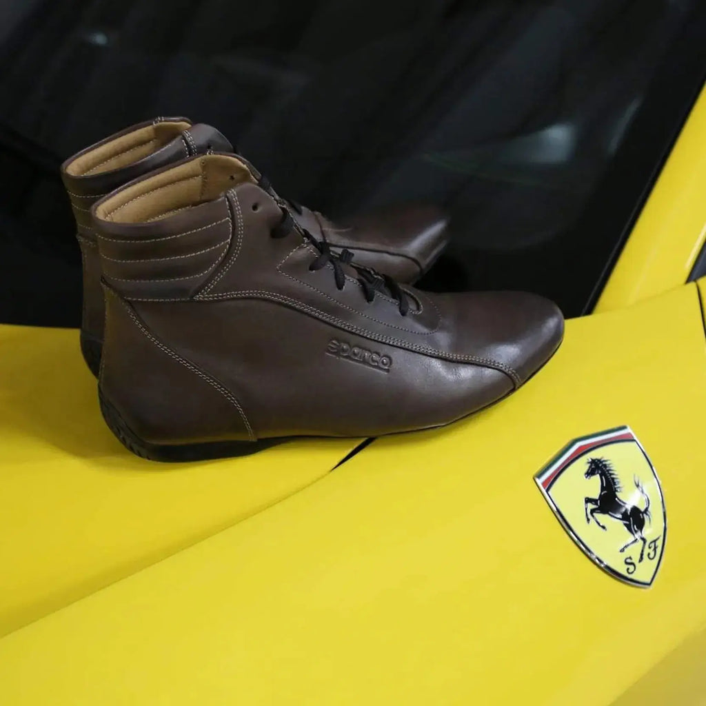 Paire de chaussures montantes Sparco Monza en cuir marron, posée sur une Ferrari