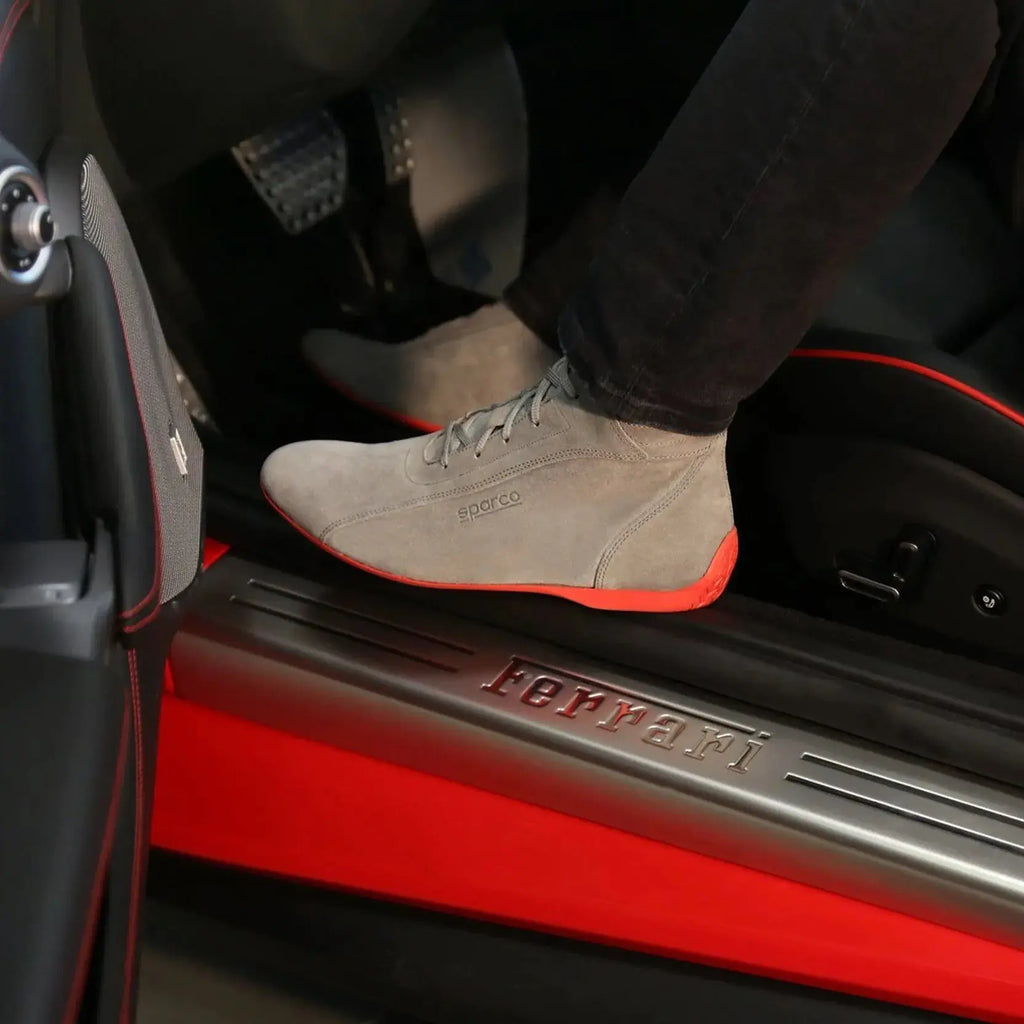 Chaussures montantes Sparco Monza en cuir suédé gris avec semelle rouge, portées à bord d'une Ferrari