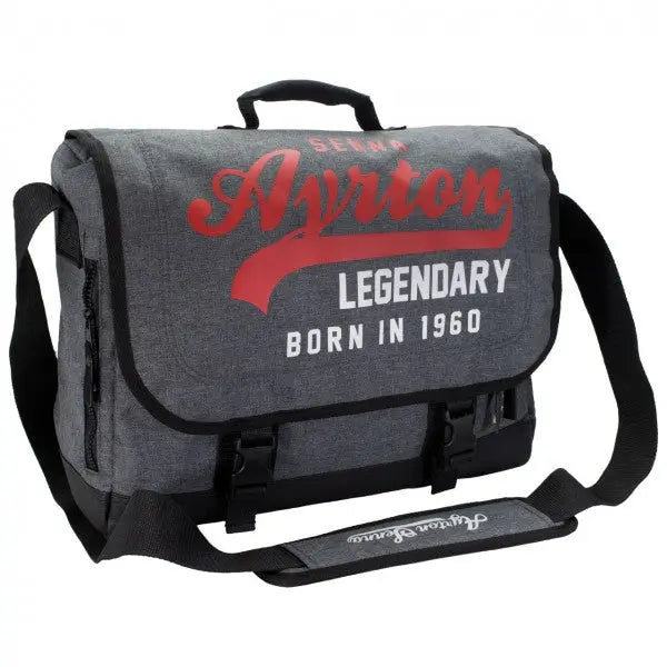 Sac Messager gris portant l'inscription Ayrton Senna  Legendary Born in 1960 en rouge blanc sur le rabat fermé par 2 boucles en plastique avec poignée sur le dessus et bandoulière portant la signature du pilote